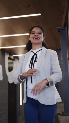 vertical video of portrait of happy biracial businesswoman in casual office, slow motion