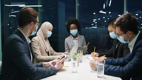 grupo de empresarios multiétnicos con máscaras médicas en una reunión de equipo en una oficina moderna y discutiendo sobre un proyecto 1