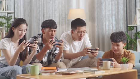 asian teen group playing game on smartphone, break time after working on online project, students with books and laptop studying at home