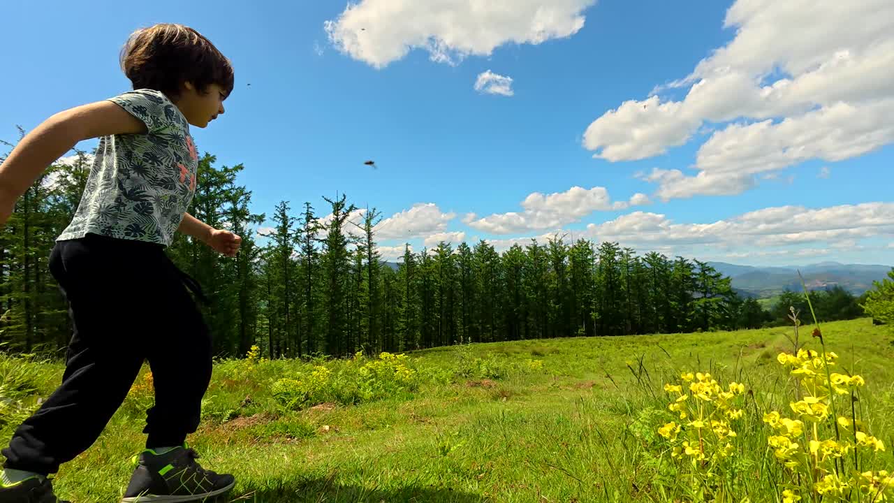 A child runs in a grassy field with trees and a blue sky