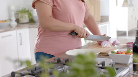 Feliz-Mujer-Birracial-De-Talla-Grande-Cortando-Verduras-En-La-Cocina-De-Casa,-Cámara-Lenta