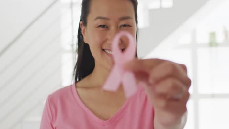 Fröhliche-Asiatische-Frau-Im-Rosafarbenen-T-Shirt,-Die-Zu-Hause-Eine-Rosa-Schleife-Zeigt