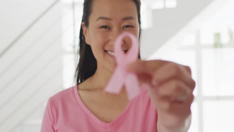 happy asian woman in pink tshirt showing pink ribbon at home