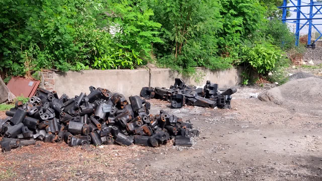 The image shows a railway depot storage area with piles of black iron train knuckle couplers stacked on the ground