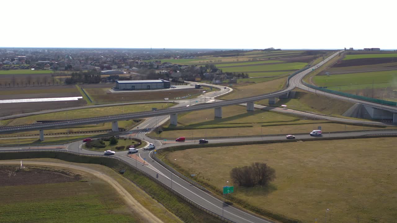 Aerial wide angle fly by shot of the vehicles approaching a roundabout in a highway on a bright sunny afternoon