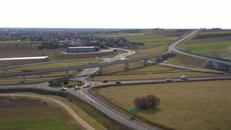aerial wide angle fly by shot of the vehicles approaching a roundabout in a highway on a bright sunny afternoon