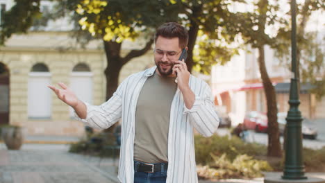 happy young caucasian man tourist in casual talking on smartphone while standing on city street