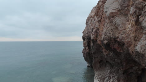 drone-flies-at-a-low-altitude-past-cliffs-and-out-over-serene-glassy-surface-of-calm-sea