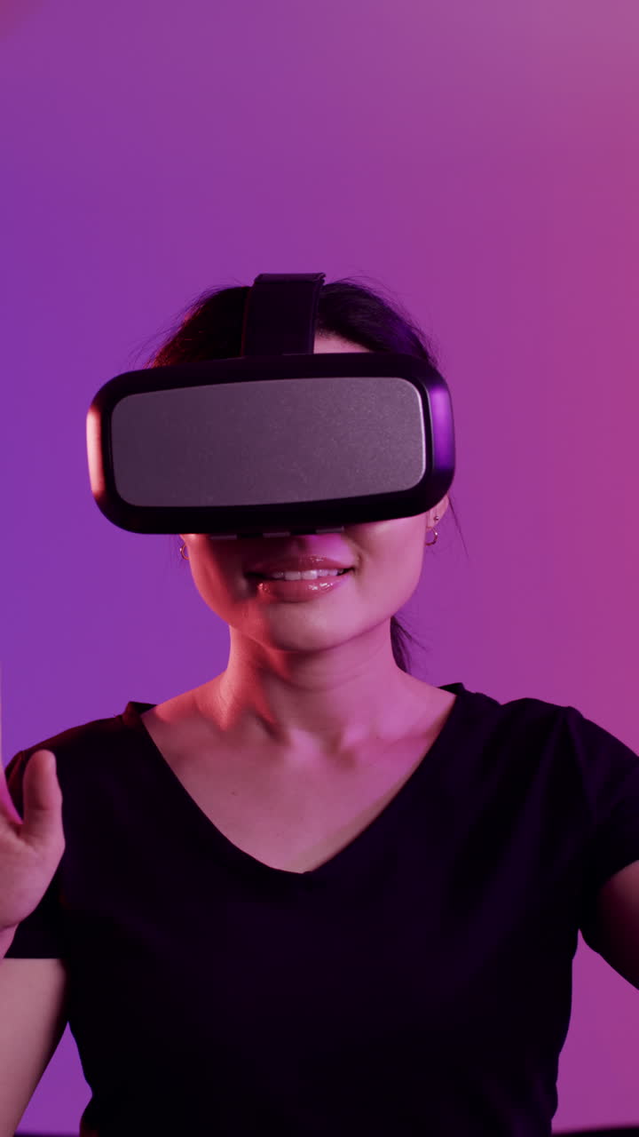 Vertical video of asian woman and woman using vr headsets on purple background, slow motion