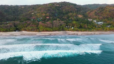 aerial above turquoise water with huge waves, beach, coastline and surfers in the pacific ocean in tamarindo, costa rica