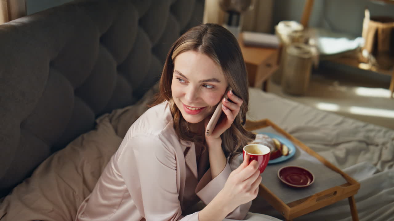 Woman having coffee and talking on the phone in bed