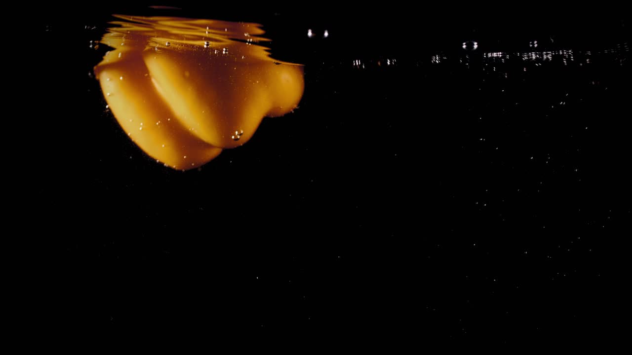 pimentón amarillo cayendo al agua con burbujas sobre fondo negro