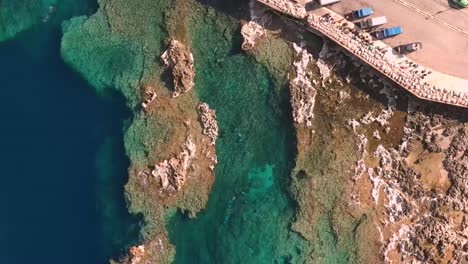 Drone-shot-rotating-downwards-towards-divers-in-the-blue-sea-in-Cirkewwa-Malta