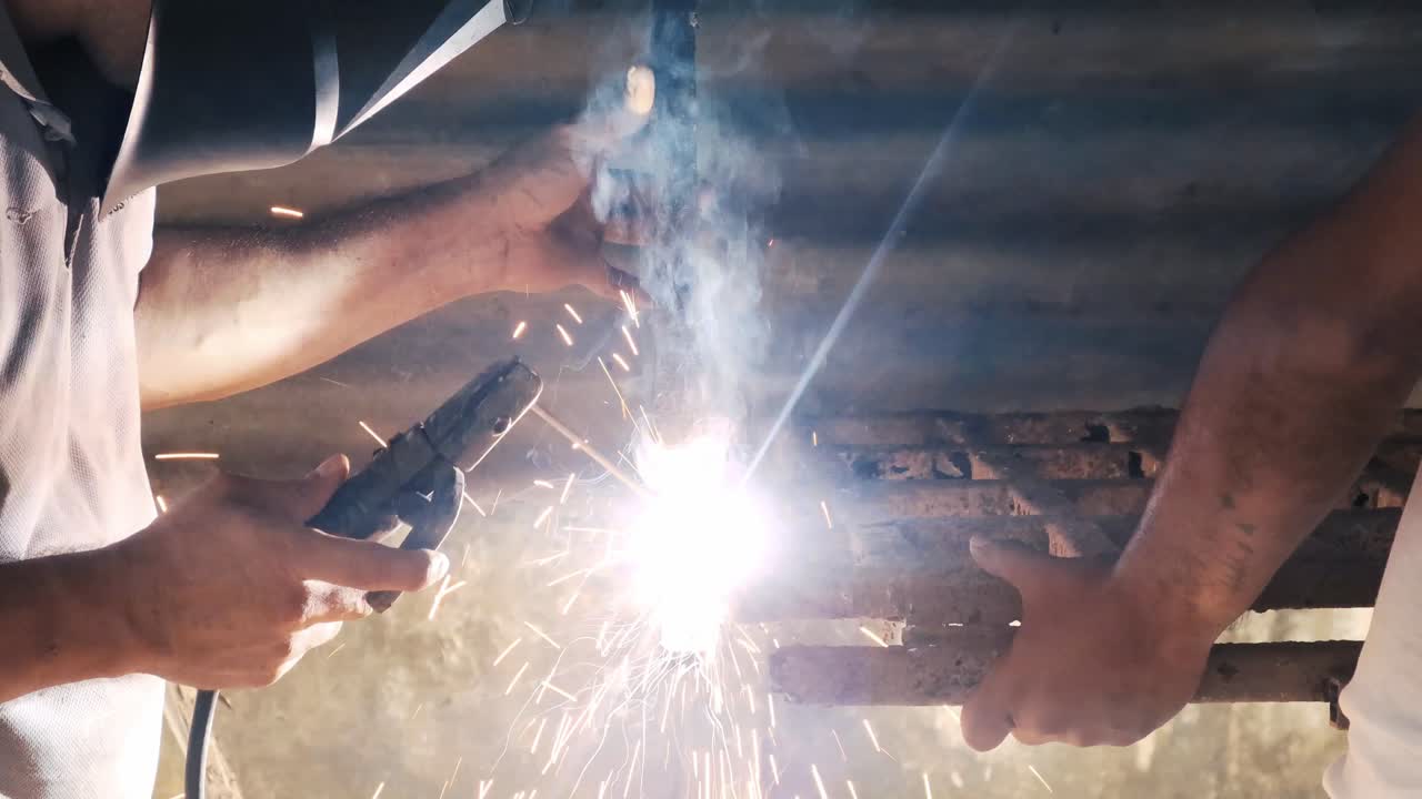 Professional welder employing industrial welding machine to put together two pieces of metal creating a metalic structure as part of his daily work at a local small business