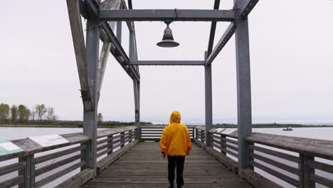 wide shot of a person in a yellow jacket walks down into a dock overlooking water