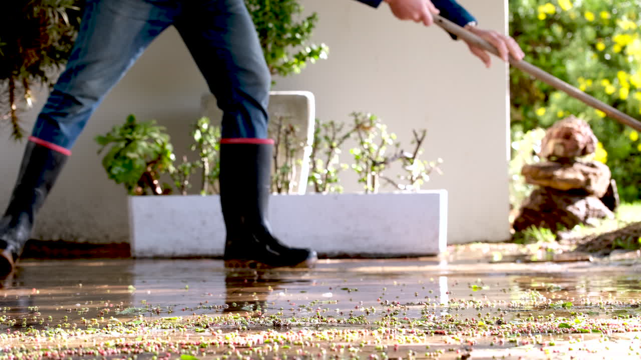 Side view of man in boots sweeping standing rainwater from driveway in winter