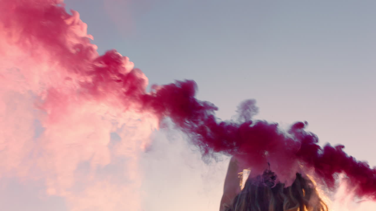 bellissima donna che agita una granata di fumo rosa che balla sulla spiaggia all'alba celebrando la libertà creativa con un gioco di movimento di danza