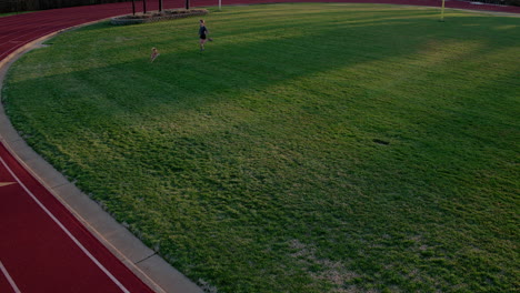 a teen girl athlete chases a dog on a high school football field