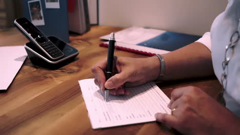 Una-Mujer-De-Negocios-Escribiendo-En-Un-Cuaderno-Blanco-En-Blanco-Sobre-La-Mesa-En-La-Oficina