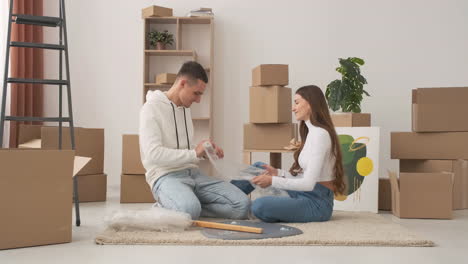 zoom in shot of young couple in a new house sitting on the floor unrolling bubble wrap 1