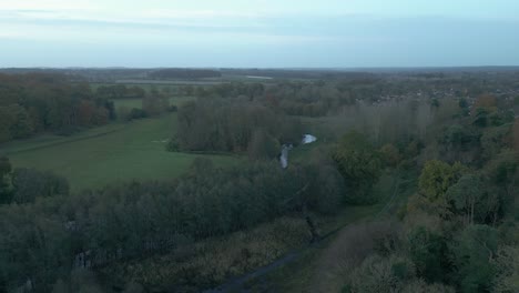 zipline aerial drone shot of the lush green trees, winding rivers, verdant fields, and a nearby village in breckland district, norfolk county, in the east of london, united kingdom