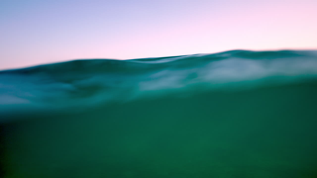 Gentle turquoise ocean waves creating soothing ripples during a stunning sunset, with soft pink and purple hues painting the sky in a tranquil and serene evening atmosphere