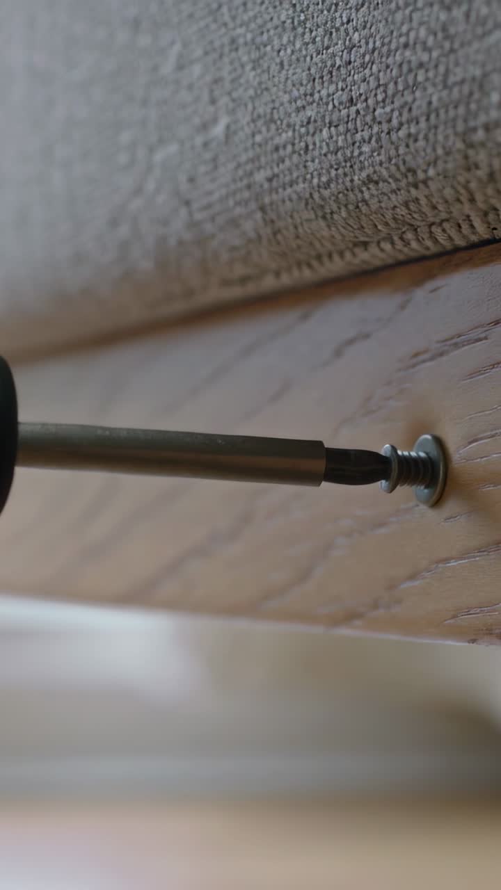 Vertical video: Contacting cross-head, bit turning screw into wood rail beneath cushion, seating