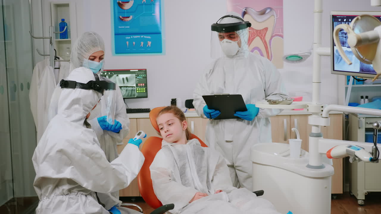 estomatólogo en traje protector midiendo la temperatura del paciente niño