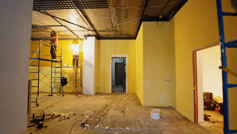 spacious interior of the room with a wide column in the middle. three workers finish the repairing of the room.