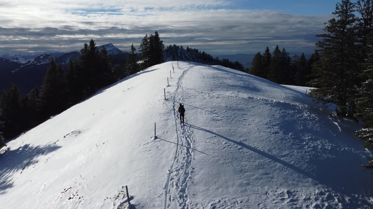Uomo che cammina su una distesa innevata con montagne sullo sfondo.