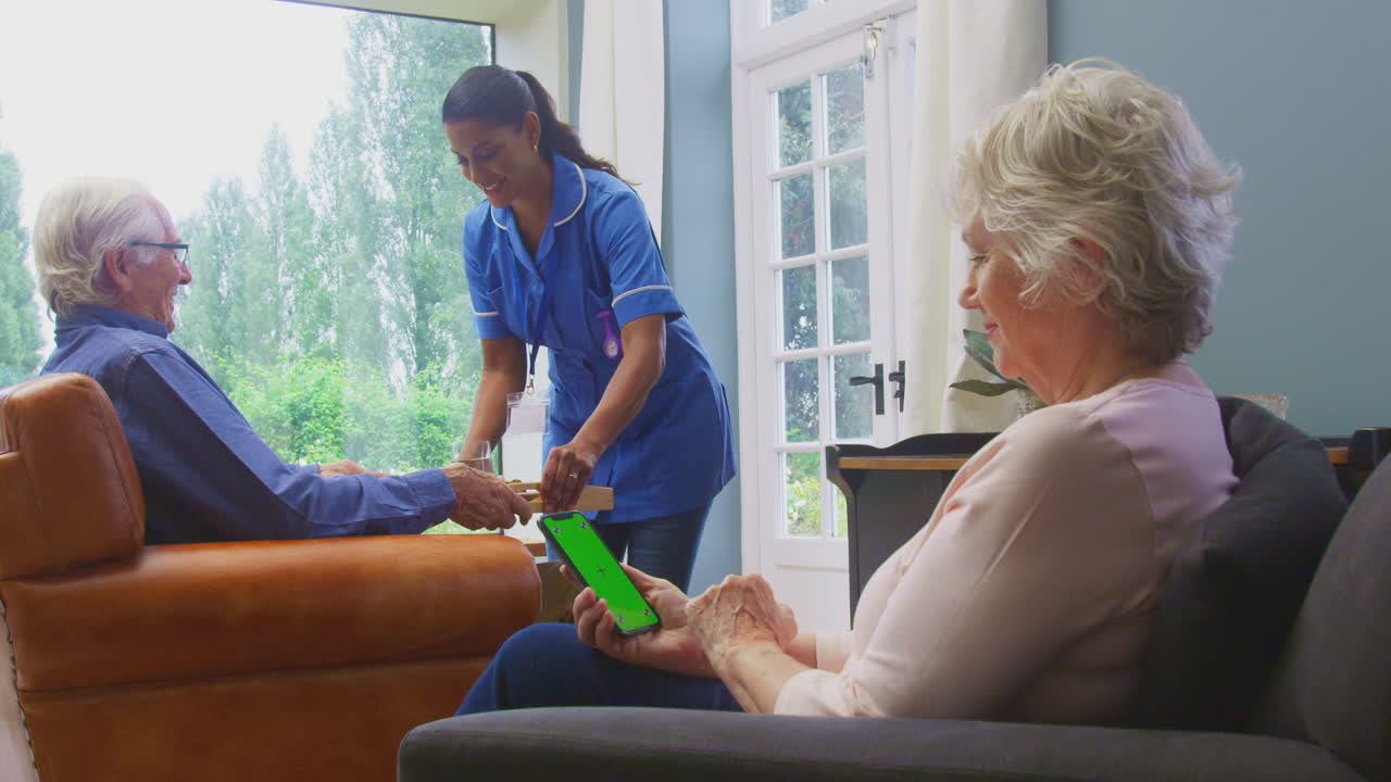 trabajadora de cuidado femenino en uniforme trayendo comida en bandeja a un hombre mayor sentado en el salón en casa