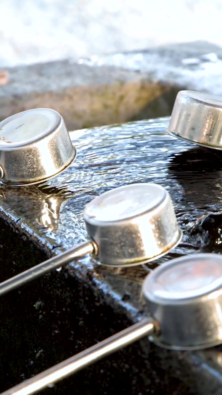 Close-up shot of metal ladles resting on a stone basin with flowing water