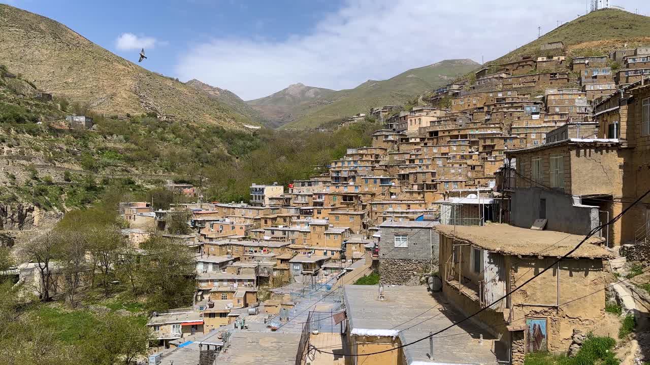 Villaggio in mattoni a gradoni, Kurdistan, pendio accidentato, Monti Zagros, cascata, pietra, architettura tradizionale, paesaggio locale, tetto culturale in terra battuta, rosso rustico, Iran, legno marrone, tramonto, ora d'oro, verde sereno.