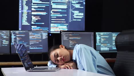 vista lateral de una programadora asiática durmiendo mientras escribe código en una computadora portátil utilizando múltiples monitores que muestran la base de datos en los escritorios de ventana de terminal en la oficina
