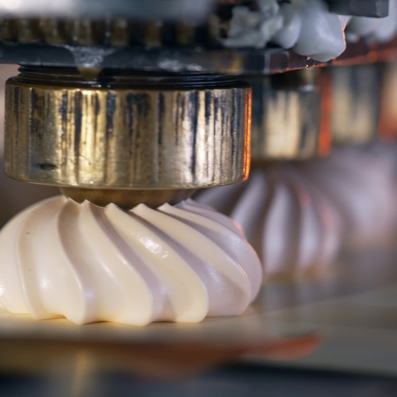 Round metal nozzles of automated machine deposit marshmallows on conveyor belt. Close up. Blurred backdrop