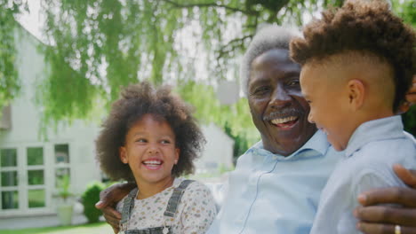 loving grandfather talking with grandchildren in garden at home