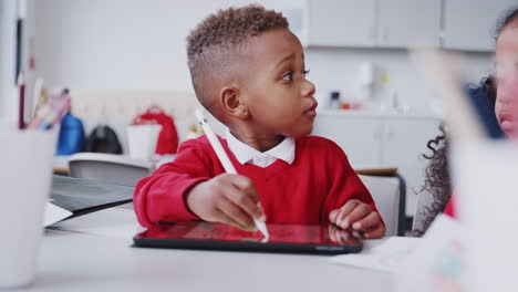 Young-schoolboy-at-a-desk-in-a-classroom-drawing-with-a-tablet-computer-and-stylus,-selective-focus