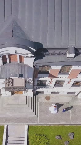 joyful bride in white dress dances with groom near dwelling building in street on nice sunny day vertical view on roof