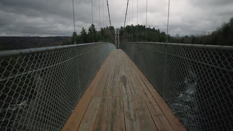 Longest-Suspended-Bridge-Above-Coaticook-River-During-Cloudy-Day-In-Eastern-Townships,-Quebec-Canada,-Tilt-Up-Shot