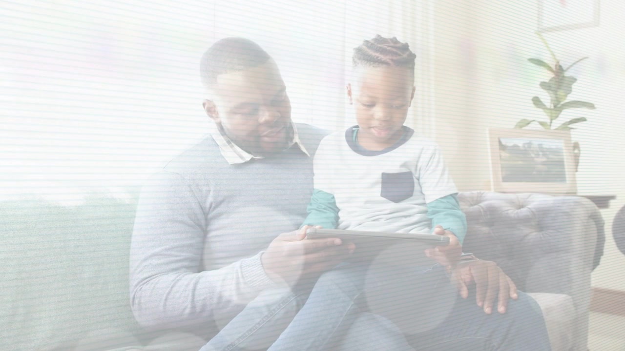 Padre che guida il figlio sul divano, inclinando il tablet mentre il bambino tocca e un'app di apprendimento mostra lo schermo