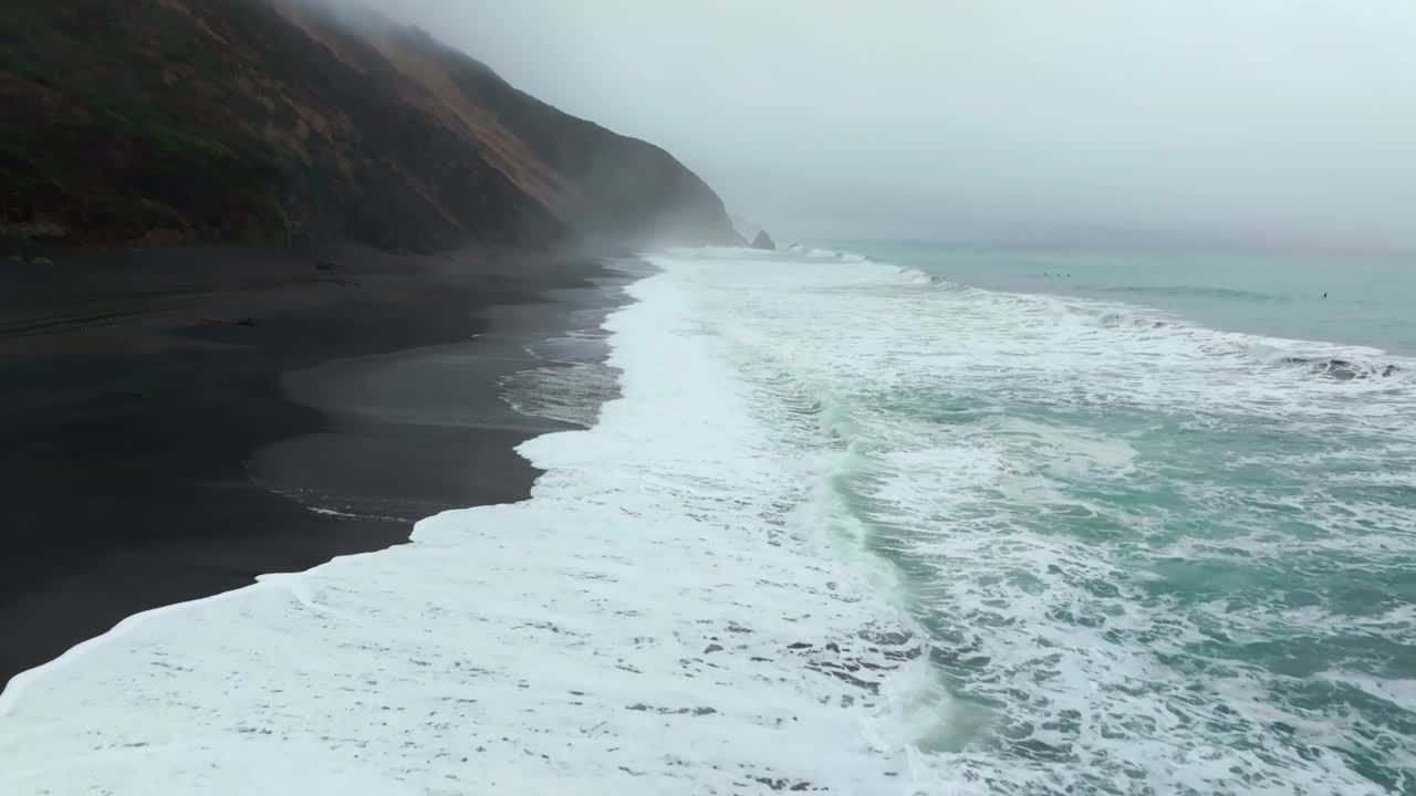 Waves crashing black sand boulder rocks rugged coastline USAL Beach Campground Lost Coast Trail California aerial drone fog mist rain cloudy layers mountainside morning Pacific Ocean forward pan up