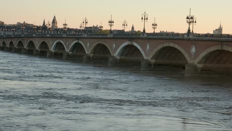 bridge with a raging river un a sunset with an orange background , and streetlight silhouettes in budeaux, france