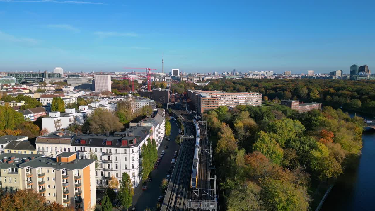 Scenic view of a train crossing a bridge over a river in berlin, surrounded by vibrant autumn foliage. fly reverse drone