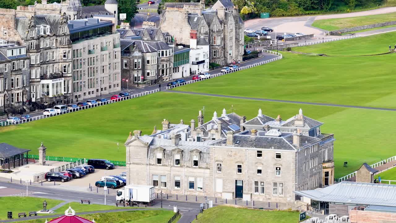Daytime aerial pan reveals classic stone clubhouse, green fairway, and historic buildings in St Andrews
