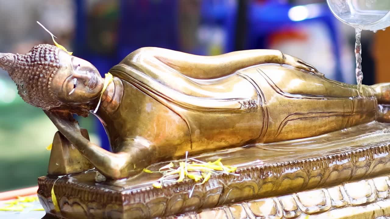 A close-up view of water being poured over a golden reclining Buddha statue, highlighting the ritualistic practice.