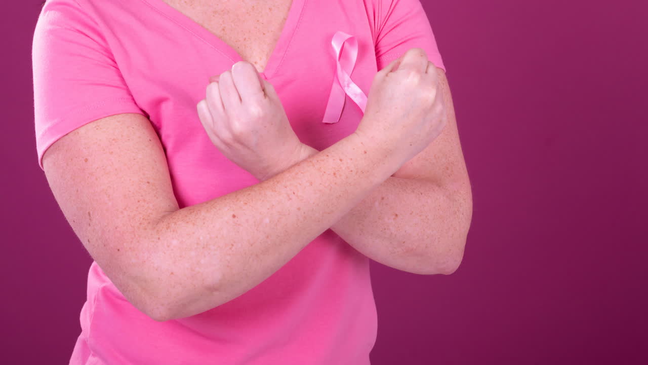 Video of midsection of caucasian woman with crossed arms wearing pink cancer awareness ribbon