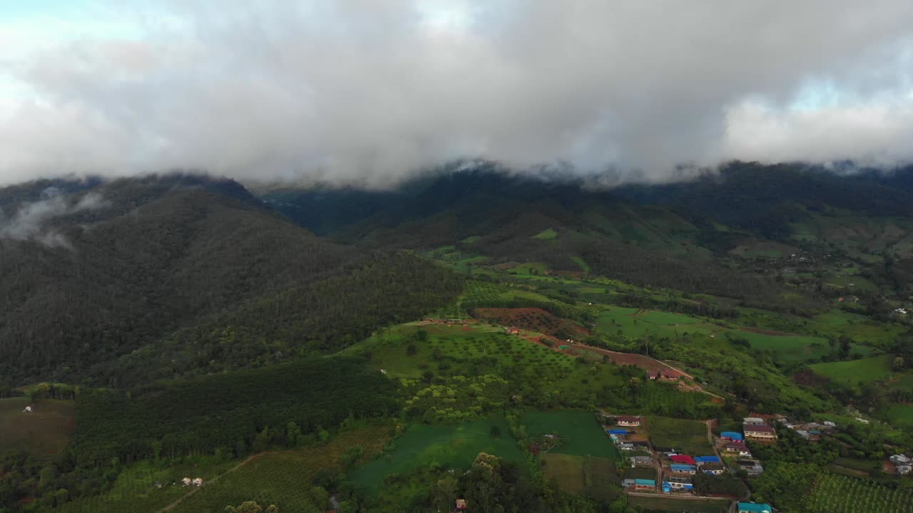 Droneflyvning over de fjerntliggende landskabsbakker i Pai, Thailand, dækket af bølgende grønne marker og tykke skyer i monsunperioden