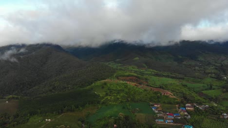 Drone-fly-over-the-remote-countryside-hills-of-Pai,-Thailand-covered-in-rolling-hills-of-green-fields-and-thick-cloud-during-monsoon-season