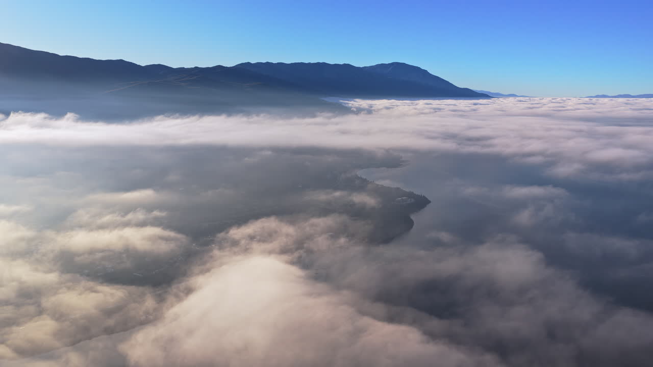 Aerial drone view of a Galichica mountain ridge rising above a sea of clouds, with soft layers of fog covering the valley below
