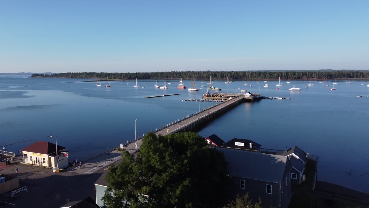 Aerial drone rising over building roofs in St-Andrews by the Sea, revealing the pier with calm waters, sunny morning
